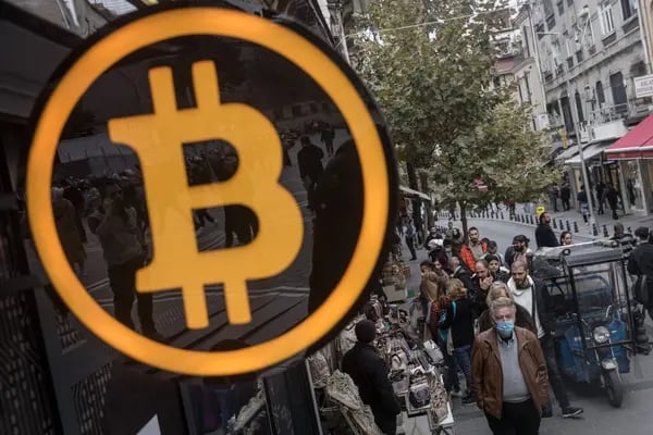 La gente pasa junto a un símbolo de Bitcoin en la entrada de una oficina de intercambio de criptodivisas el 19 de octubre de 2021 en Estambul, Turquía.