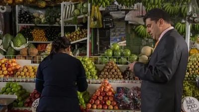 Un hombre revisa su lista de compras mientras un trabajador selecciona frutas.