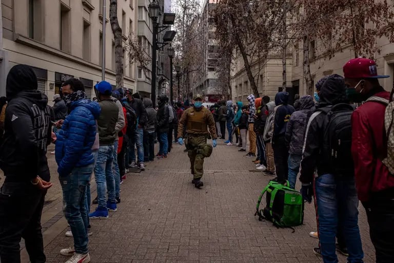 Un oficial de policía con máscaras protectoras camina entre una fila de personas que esperan afuera de una oficina de administración de fondos de pensiones en Santiago, Chile, el lunes 27 de julio de 2020.dfd