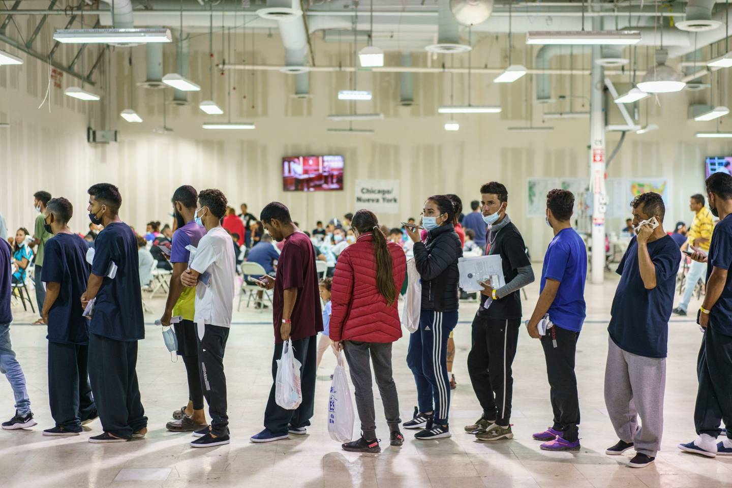 Migrantes esperan en una fila para abordar micros hacia Nueva York y Chicago
