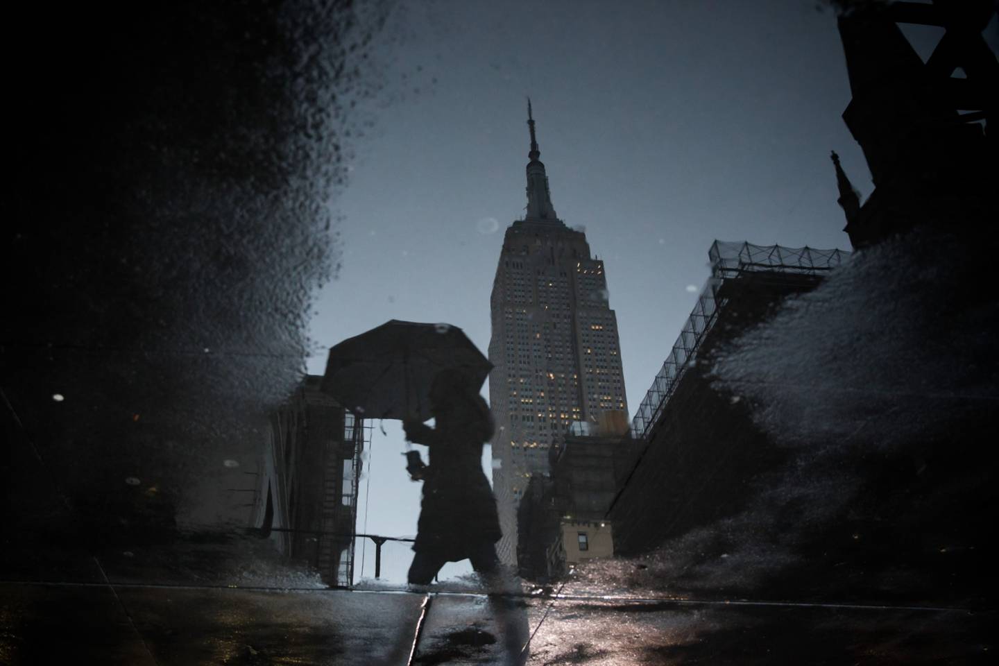 Un peatón lleva un paraguas mientras pasa por delante del Empire State Building se refleja en un charco en Nueva York, EE.UU., el viernes 3 de enero de 2020. Fotógrafo: Michael Nagle/Bloomberg