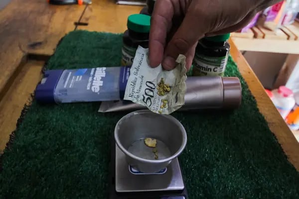 Un cliente coloca oro envuelto en un billete de bolívares arrugado en una balanza para el pago en una farmacia en Tumeremo, Venezuela.Fotógrafo: William Urdaneta / Bloomberg