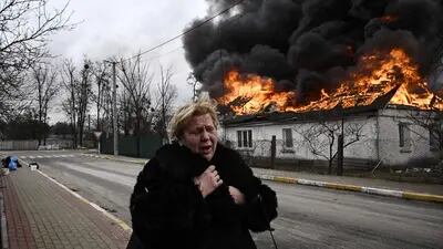 Uma mulher está perto de uma casa em chamas em Irpin, nos arredores de Kiev, em 4 de março.Fotógrafo: Aris Messinins/AFP/Getty Images