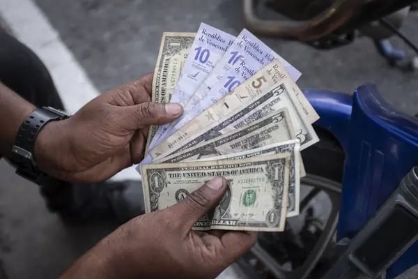 Un vendedor sostiene billetes venezolanos y estadounidenses para una foto en el barrio de Petare de Caracas, Venezuela, el jueves 17 de agosto de 2023.