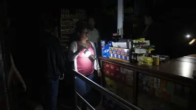 Una mujer sostiene una lámpara mientras los clientes se preparan para comprar comestibles en una tienda de conveniencia, durante un apagón en Caracas, Venezuela, el lunes 22 de julio de 2019. 
