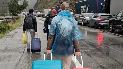 Personas con equipaje pasan junto a vehículos con matrícula rusa en el lado ruso de la frontera hacia el puesto de control aduanero de Nizhniy Lars entre Georgia y Rusia, el 25 de septiembre.