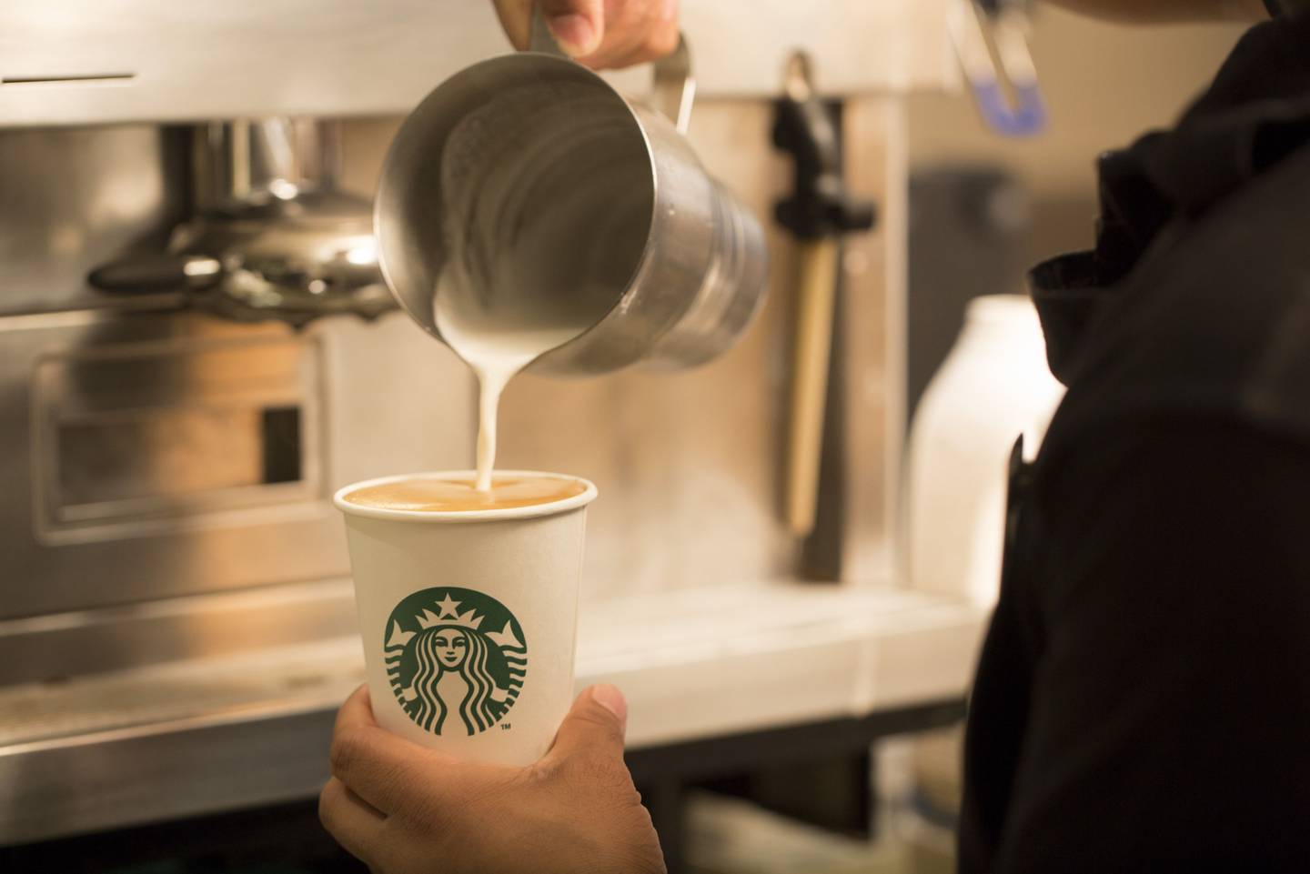 An employee pours milk into a cardboard coffee cup inside a Starbucks Corp. coffee shop in London, U.K., on Monday, June 9, 2014. U.K. Photographer: Jason Alden/Bloomberg