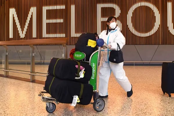 Una viajera internacional con ropa protectora y mascarilla en el aeropuerto de Melbourne.