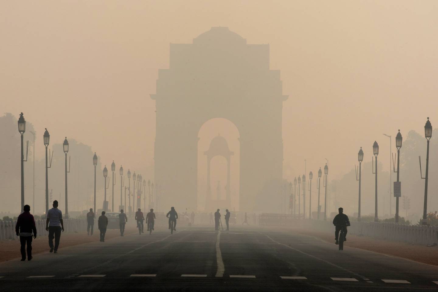 Pedestrians walk along Rajpath boulevard as India Gate monument stands shrouded in smog in New Delhi, India, on Tuesday, Nov. 5, 2019.