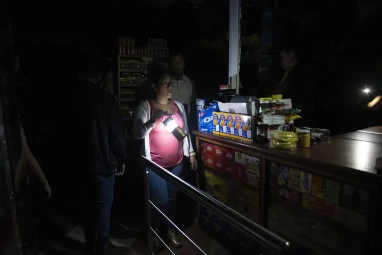 Una mujer sostiene una lámpara mientras los clientes se preparan para comprar comestibles en una tienda de conveniencia, durante un apagón en Caracas, Venezuela, el lunes 22 de julio de 2019. dfd