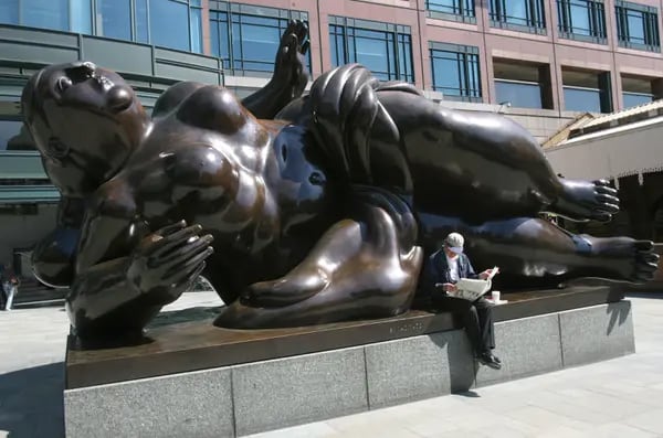 Un hombre lee un periódico sentado en una escultura pública titulada ''Broadgate Venus'' de Fernando Botero en Londres, Reino Unido.