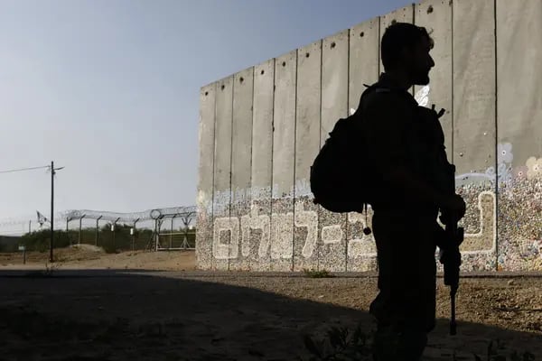 Un soldado israelí patrulla junto a una barrera protectora de seguridad decorada con la leyenda "Sendero para la Paz" cerca de la valla fronteriza con la Franja de Gaza, a la izquierda, en el moshav Netiv HaAsara, en el sur de Israel, el viernes 17 de noviembre de 2023. Fotógrafo: Kobi Wolf/Bloomberg
