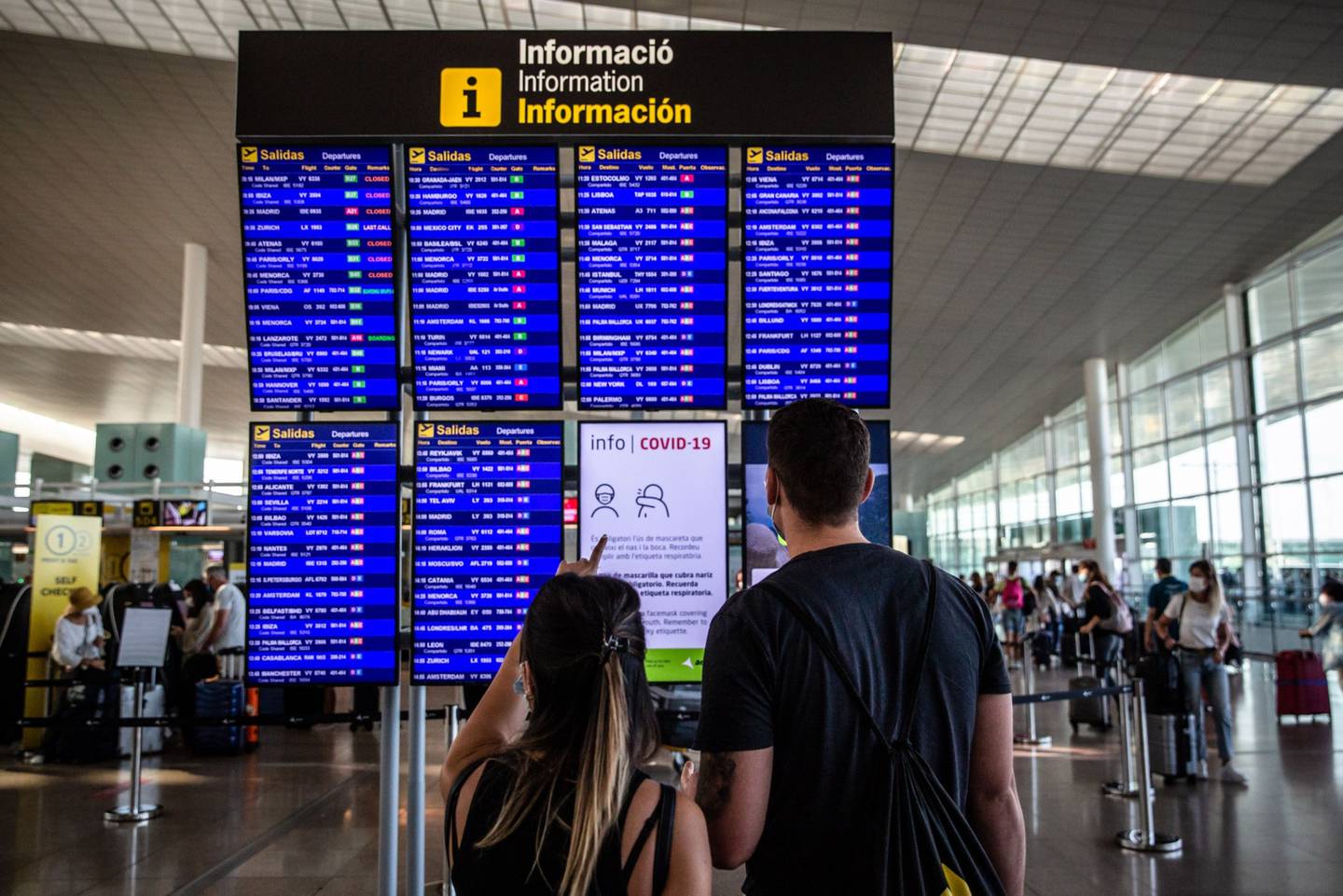 Passengers check the flight information boards in El Prat airport, operated by Aena SA, in Barcelona, Spain, on Monday, Aug. 2, 2021.