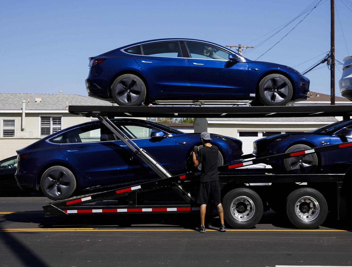 Los trabajadores descargan los vehículos eléctricos Tesla Model 3 de un transportador de automóviles fuera del centro de entrega de la compañía en Marina Del Rey, California.