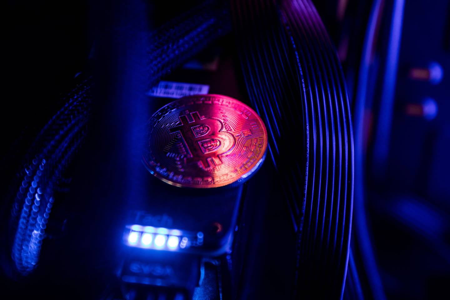 Un token que representa la moneda virtual bitcoin se encuentra entre los cables y la iluminación LED dentro de una computadora de "plataforma de minería" en esta fotografía arreglada en Budapest, Hungría, el miércoles 31 de enero de 2018.dfd