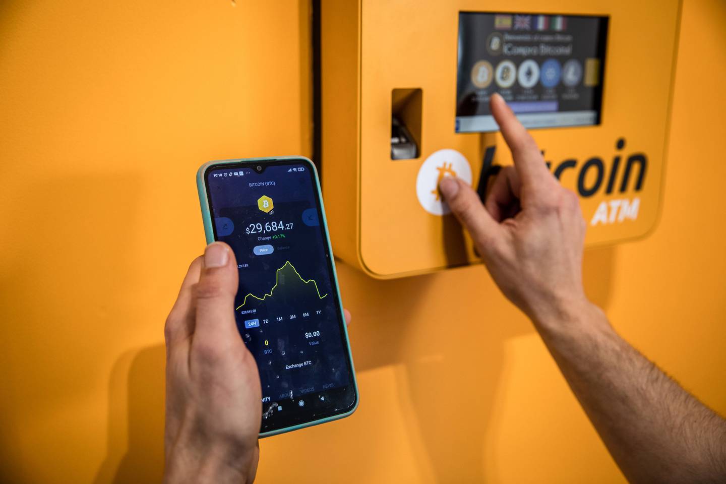 Un cliente inspecciona un gráfico de precios de bitcoin mientras utiliza un cajero automático de criptomonedas (ATM).dfd