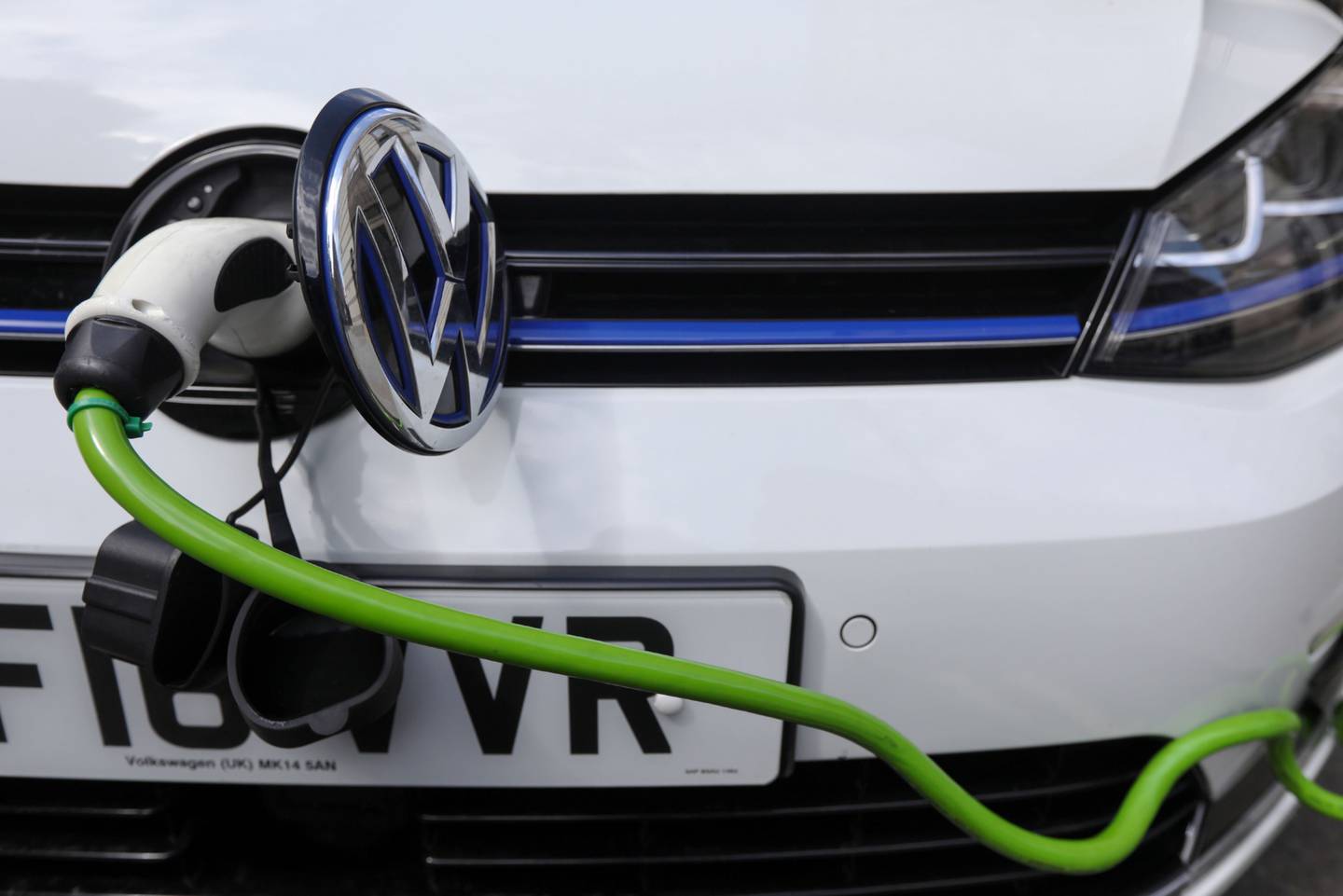 A charging plug sits next to a VW badge cover in the port of a Volkswagen AG GTE Golf hybrid automobile at a charging station in London U.K.