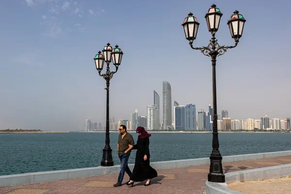 casal caminha ao longo da Corniche com arranha-céus comerciais e residenciais ao fundo em Abu Dhabi, Emirados Árabes Unidos