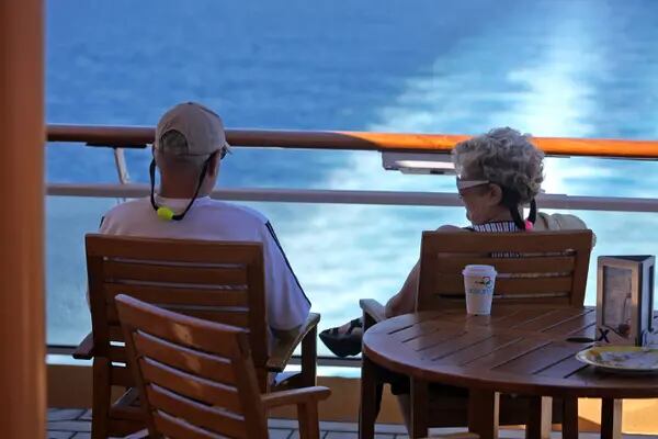 Dos pasajeros se sientan en sillas de madera a lo largo de la barandilla y miran al mar en el Sunset Bar en el Mar Caribe, cerca de la costa de Cuba.