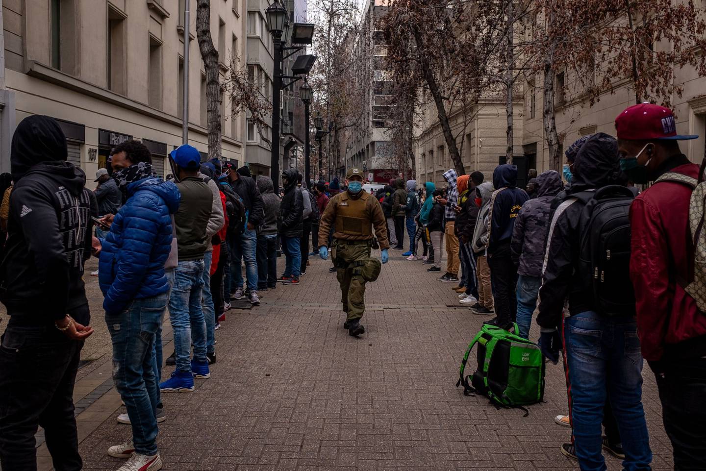 Un oficial de policía con máscaras protectoras camina entre una fila de personas que esperan afuera de una oficina de administración de fondos de pensiones en Santiago, Chile, el lunes 27 de julio de 2020.dfd