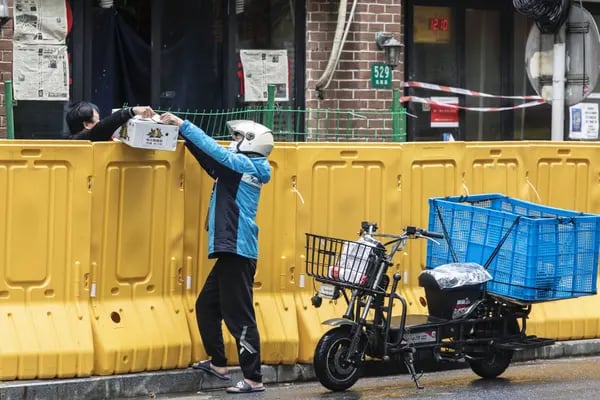 Un repartidor entrega un pedido sobre una valla, en Shanghái el 13 de mayo.