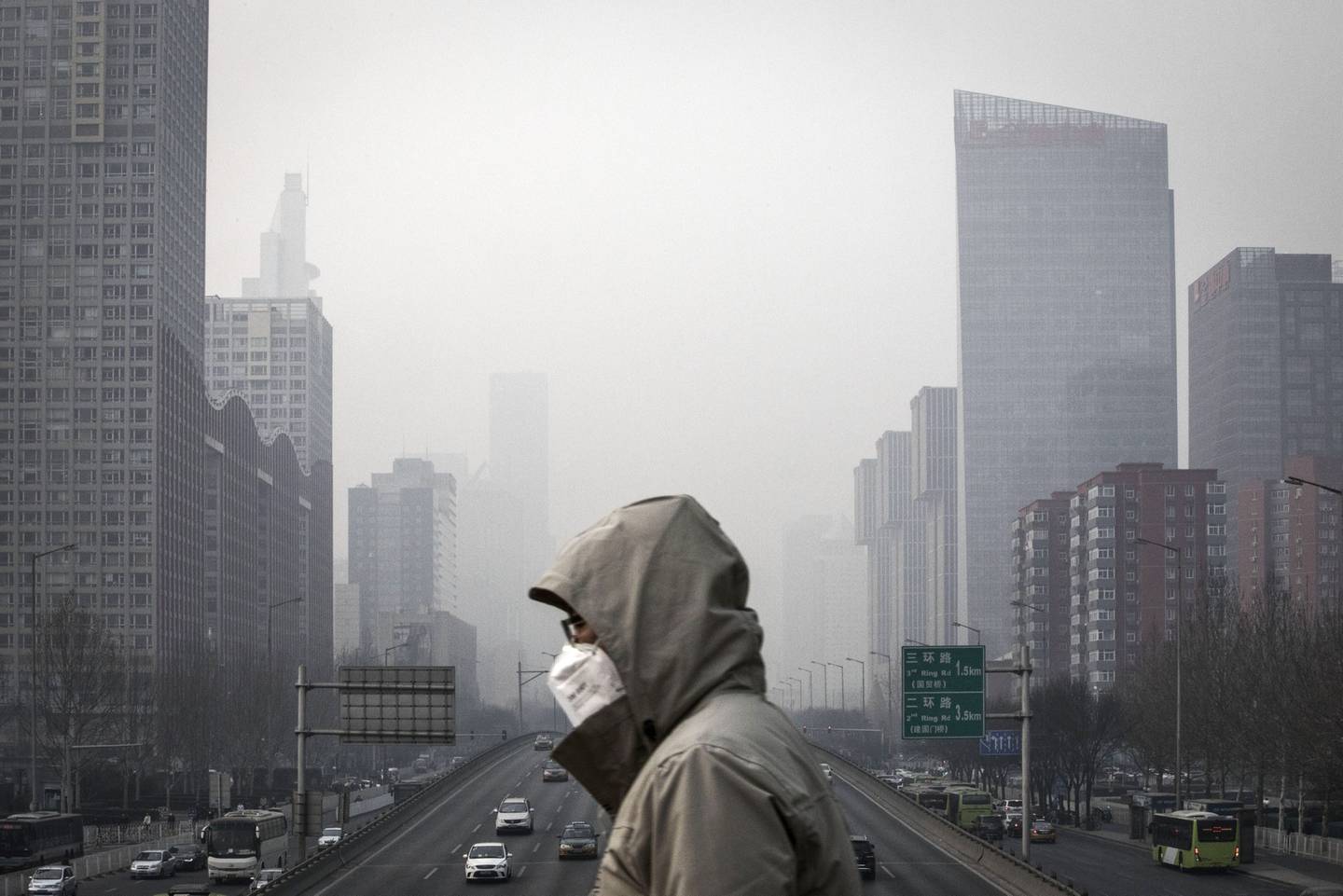 A man wearing a face mask walks on a footbridge as buildings shrouded in haze stands in the background in Beijing.