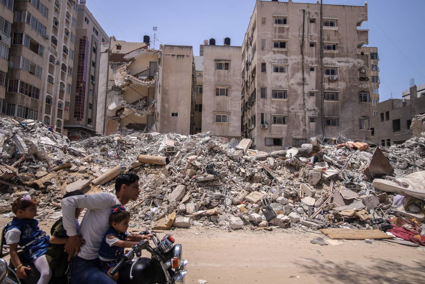 Un motociclista lleva a unos niños junto a edificios residenciales destruidos en la ciudad de Gaza el 21 de mayo de 2023
