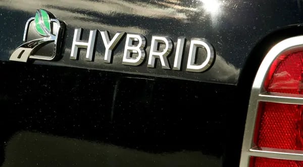Foto da traseira de um carro em close. A lataria é preta e é possível ler em prata a palavra "Hybrid" (híbrido)