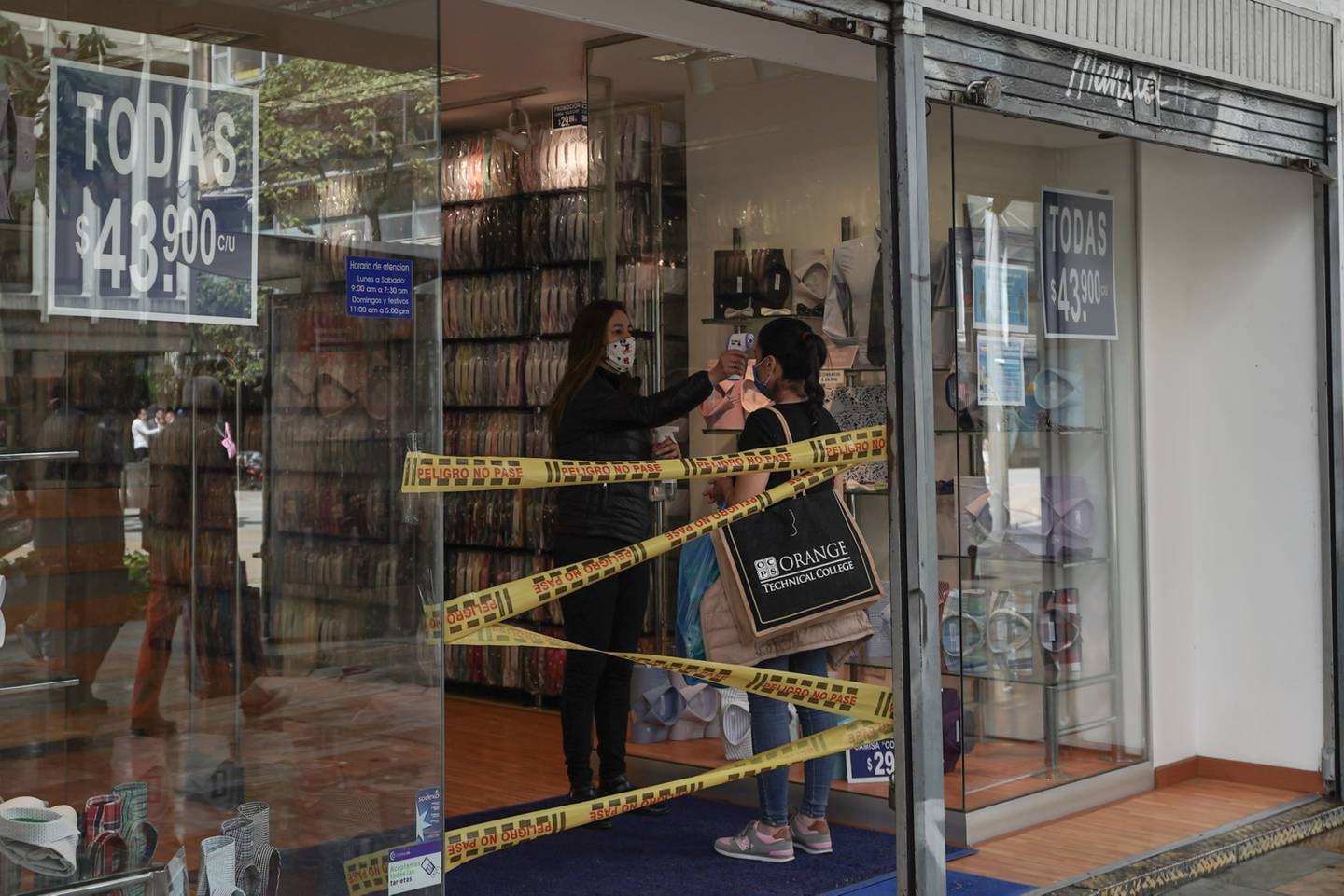 Un trabajador con una máscara protectora toma la temperatura de un cliente en una tienda de ropa en el centro de Bogotá, Colombia, el martes 16 de junio de 2020.