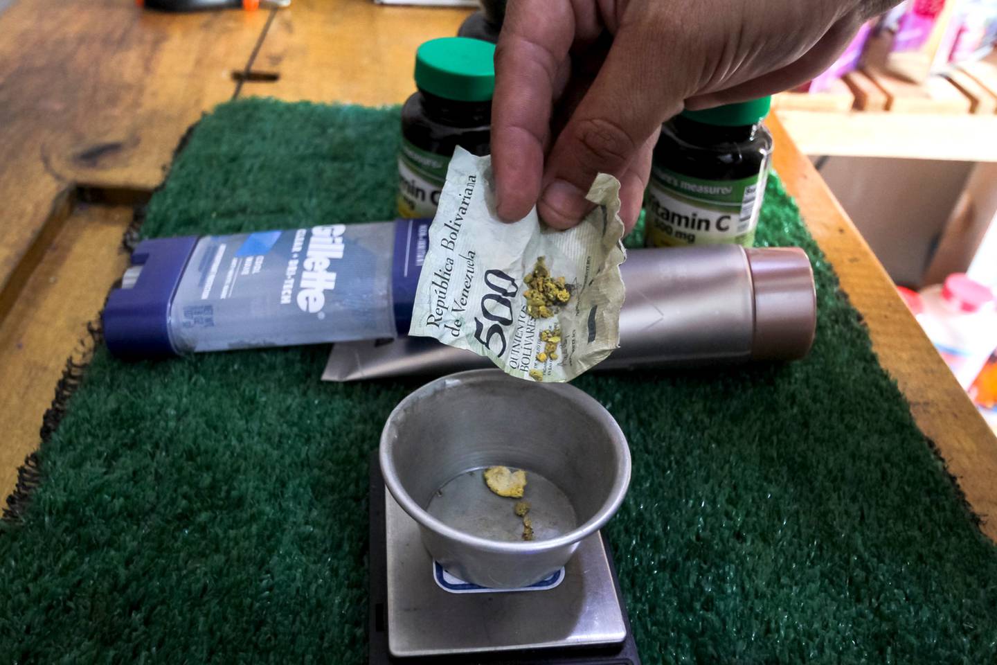 Cliente coloca ouro embrulhado em uma nota de bolívar amassada em uma balança para pagamento em uma farmácia em Tumeremo, dfd