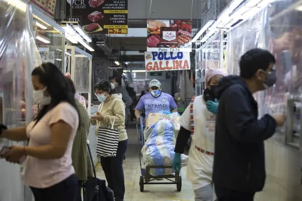 Los compradores compran carne de un carnicero en un mercado en Lima, Perú.