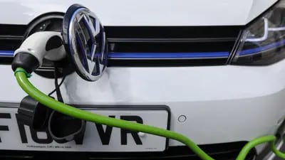 A charging plug sits next to a VW badge cover in the port of a Volkswagen AG GTE Golf hybrid automobile at a charging station in London U.K.