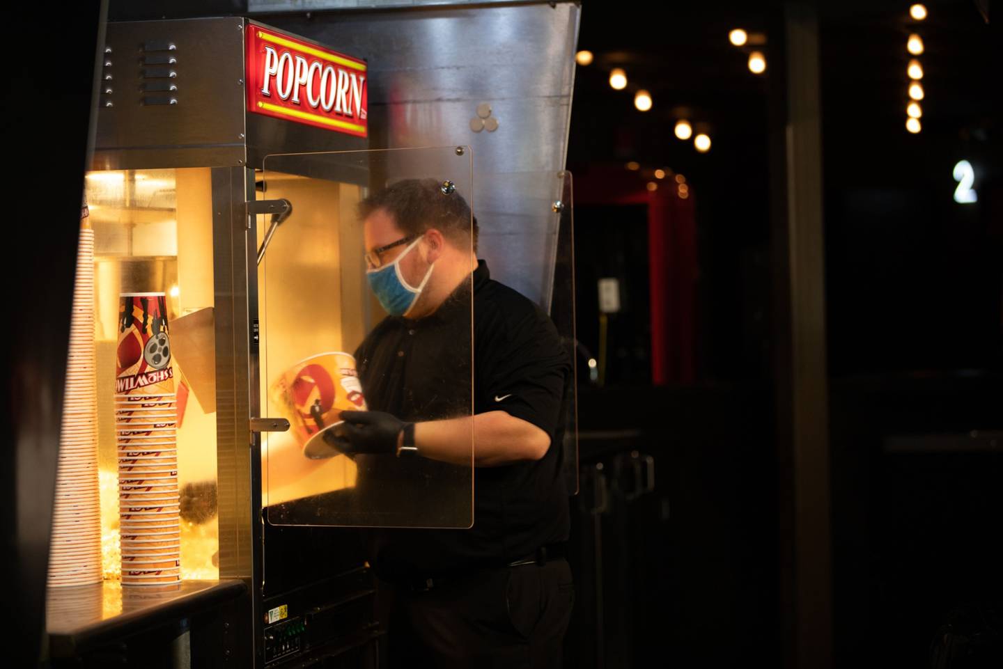 Un empleado con mascarilla y guantes de protección llena un cubo de palomitas para un cliente en el Maple Theater de Bloomfield Township, Michigan.