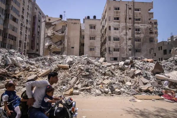 Un motociclista lleva a unos niños junto a edificios residenciales destruidos en la ciudad de Gaza el 21 de mayo de 2023