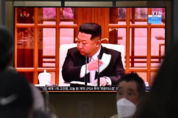 La gente se sienta cerca de una pantalla que muestra una emisión de noticias en una estación de tren en Seúl el 12 de mayo de 2022, del líder de Corea del Norte, Kim Jong Un, quitándose una mascarilla en la televisión.