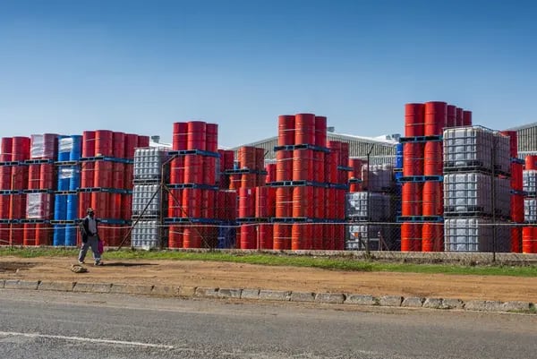 A pedestrian wearing a protective face mask walks by oil barrels stacked beyond security fencing at a facility in the Alrode district of Johannesburg, South Africa, on Tuesday, April 21, 2020. The oil meltdown accelerated, with huge losses sweeping through markets as the world runs out of places to store unwanted crude and grapples with negative pricing. Photographer: Waldo Swiegers/Bloomberg