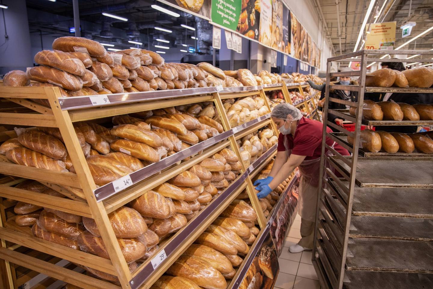 Un trabajador ubica el pan recién horneado en la sección de panadería dentro de un hipermercado.