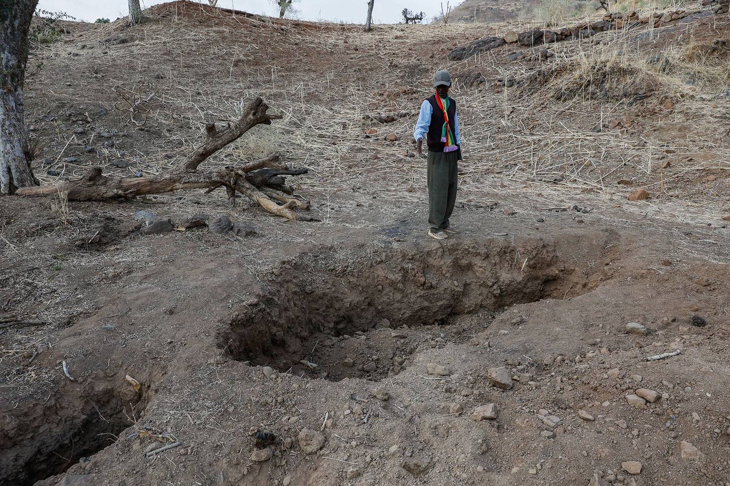 Addisu Mamaye Ayane se encuentra de pie juntos a varios agujeros grandes que marcan las ubicaciones de las fosas comunes, todos en total, contienen los restos de 36 personas asesinadas por el TPLF que están en proceso de ser excavadas en la ciudad de Adi Selam el 07 de abril de 2022 en Welkait, Etiopía.