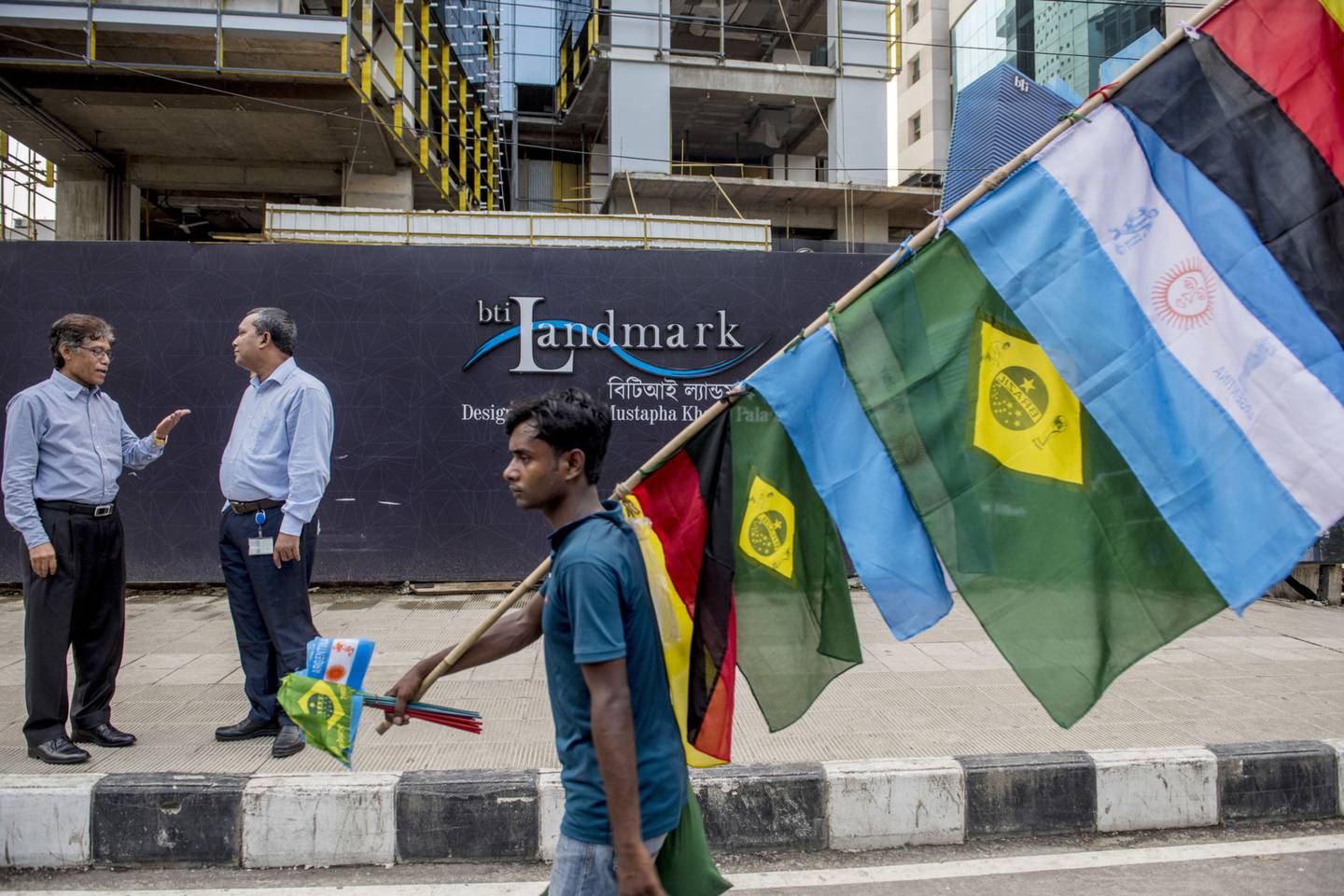 Un vendedor de banderas antes de la Copa Mundial de la FIFA Rusia 2018 pasa por delante de una obra en Dhaka, Bangladesh, el miércoles 6 de junio de 2018. La economía de Bangladés se expandirá un 6,9% este ejercicio y un 6,8% en 2019, según una encuesta realizada por Bloomberg News. Fotógrafo: Ismail Ferdous/Bloomberg