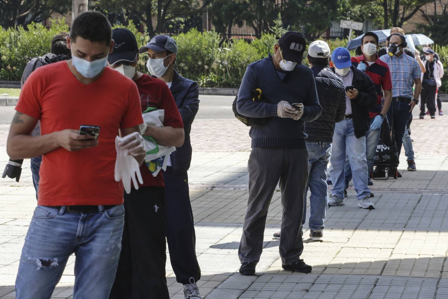 Hombres con máscaras protectoras hacen fila, mientras practican el distanciamiento social, frente a un centro comercial en Bogotá, Colombia, el lunes 13 de abril de 2020.