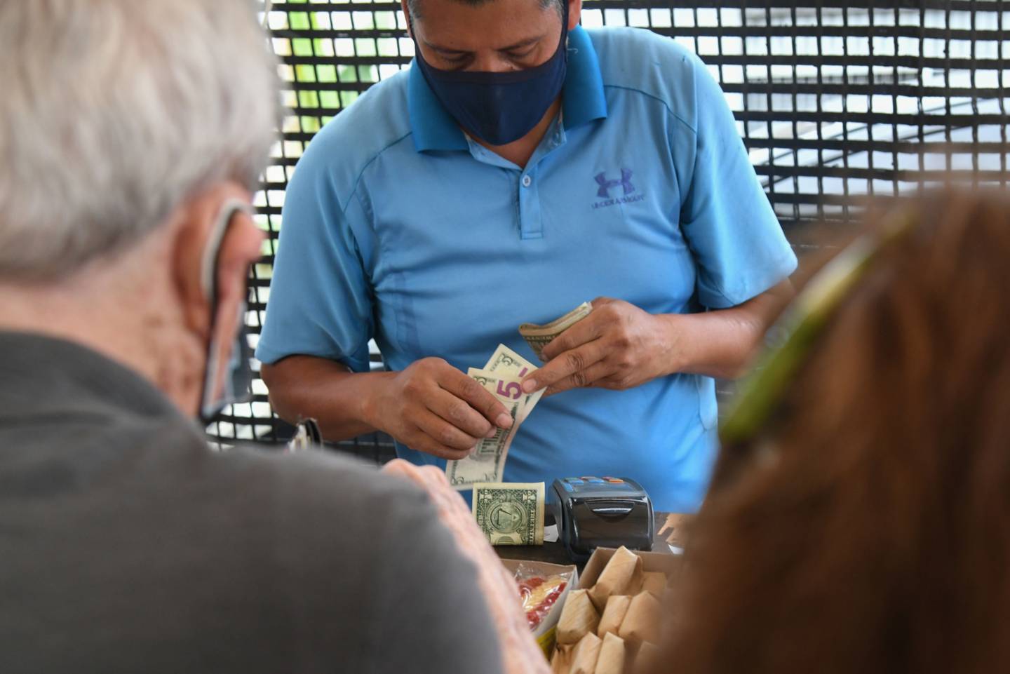 Un vendedor cuenta dólares estadounidenses mientras atiende a un cliente en un mercado de Caracas, Venezuela.