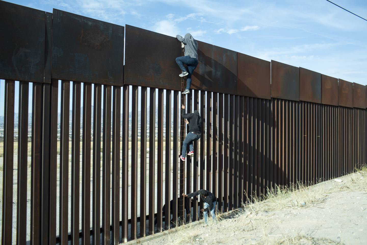 Migrantes intentan escalar el muro en la frontera entre México y Estados Unidos.