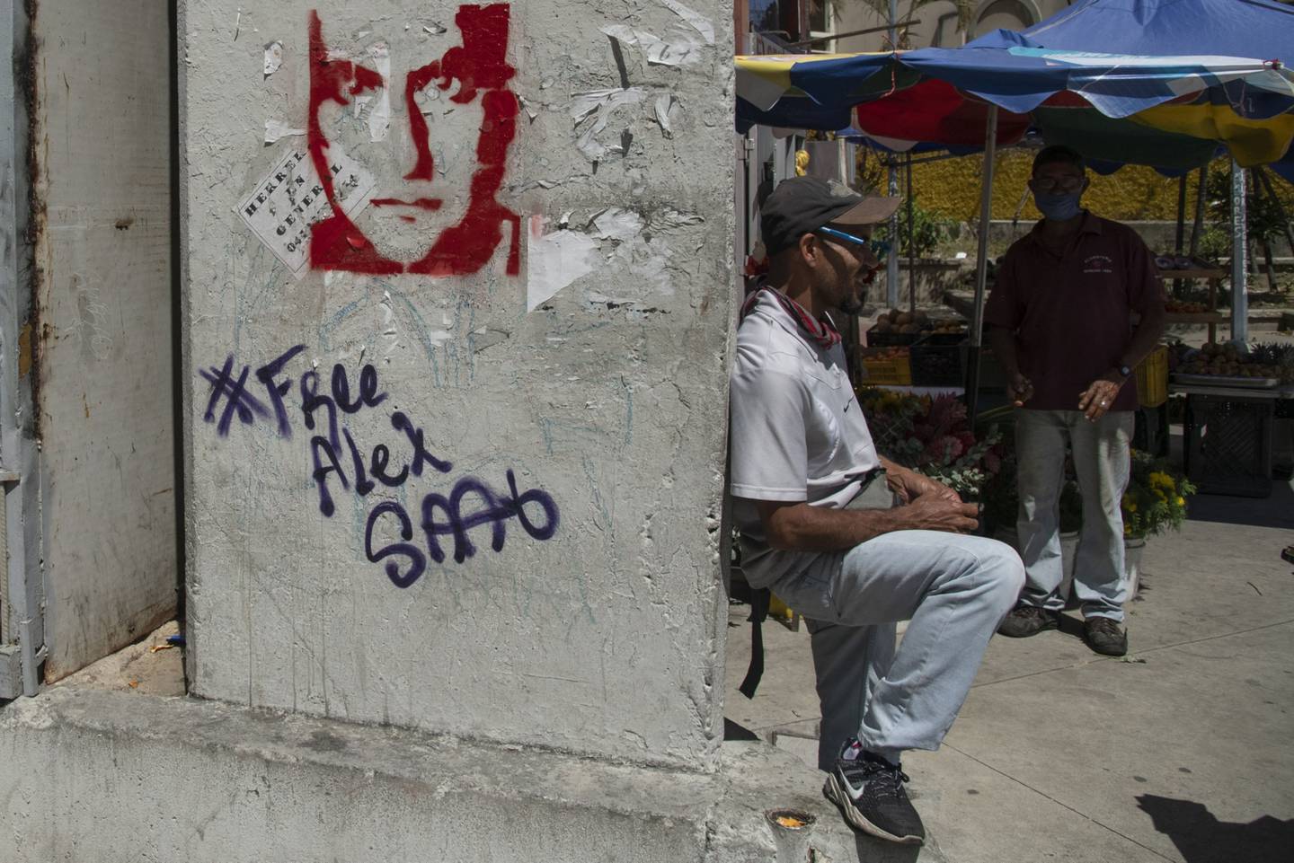 Un vendedor se sienta junto a una pared con un graffiti que dice "Liberen a Alex Saab", en el Centro de Caracas, Venezuela, el jueves 4 de febrero de 2021.dfd