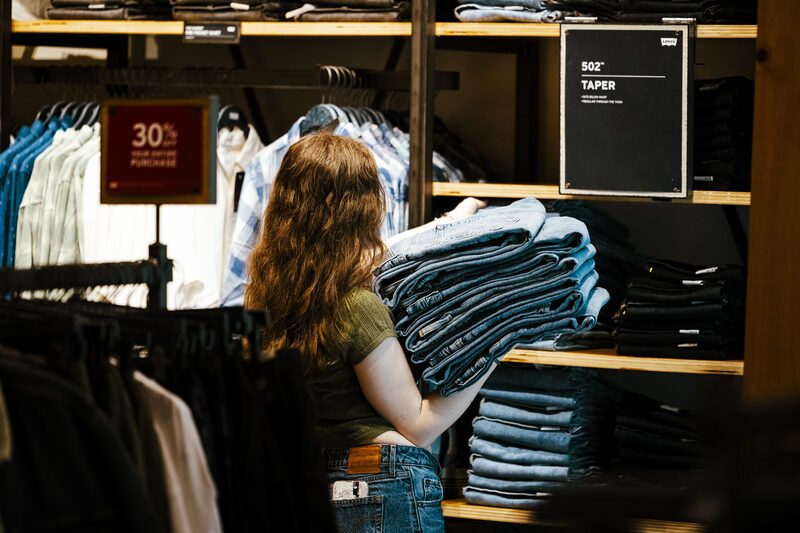 Mulher carregando peças de jeans dobradas, prestes a colocar em uma estante Mulher carregando peças de jeans dobradas, prestes a colocar em uma estante