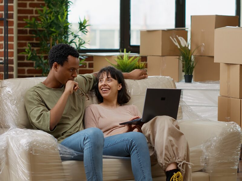Diverse couple browsing internet to buy decor on laptop, buying home furniture on online shopping to decorate living room apartment. Moving in rented household property together. Tripod shot. Diverse couple browsing internet to buy decor on laptop, buying home furniture on online shopping to decorate living room apartment. Moving in rented household property together. Tripod shot.