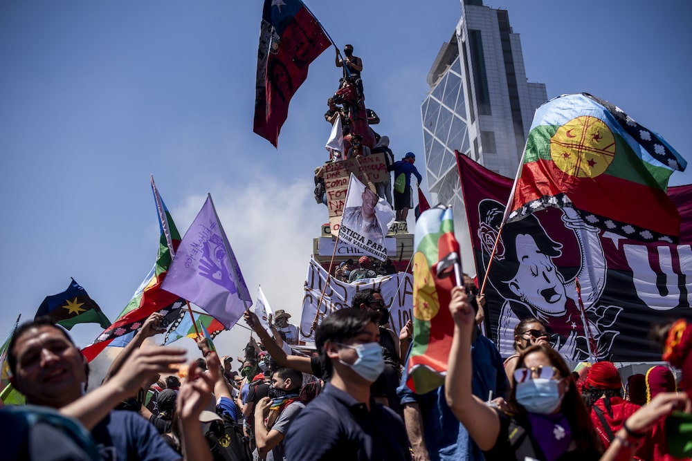 Manifestantes ondean banderas indígenas chilenas y mapuche durante una protesta en la Plaza Italia en Santiago, Chile, el domingo 18 de octubre de 2020. Este domingo se cumplió el primer aniversario de las protestas que sacudieron a Chile y como parte de un acuerdo para poner fin a los disturbios. , Los chilenos votarán este mes si deben deshacerse de su constitución, un legado de la dictadura de Pinochet en los años 70 y 80, y redactar una nueva. La nueva carta podría allanar el camino para las reparaciones y la devolución de tierras al pueblo mapuche. Manifestantes ondean banderas indígenas chilenas y mapuche durante una protesta en la Plaza Italia en Santiago, Chile, el domingo 18 de octubre de 2020. Este domingo se cumplió el primer aniversario de las protestas que sacudieron a Chile y como parte de un acuerdo para poner fin a los disturbios. , Los chilenos votarán este mes si deben deshacerse de su constitución, un legado de la dictadura de Pinochet en los años 70 y 80, y redactar una nueva. La nueva carta podría allanar el camino para las reparaciones y la devolución de tierras al pueblo mapuche.