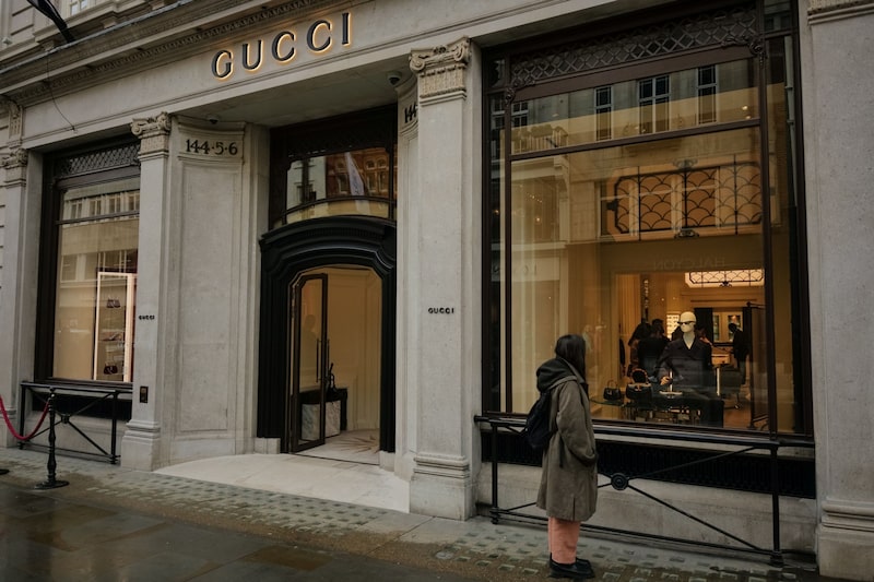 Imagem da fachada de uma loja da Gucci com uma mulher me primeiro plano olhando a vitrine Imagem da fachada de uma loja da Gucci com uma mulher me primeiro plano olhando a vitrine