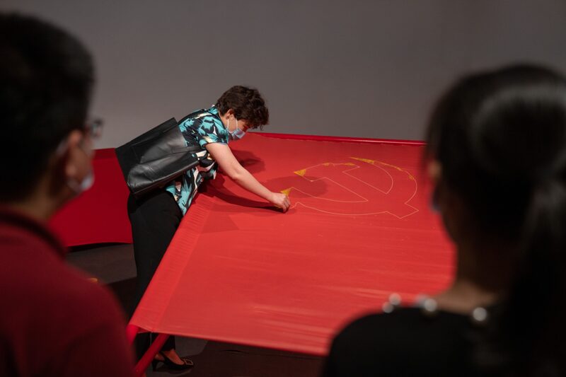 Una mujer con una mascarilla borda el emblema del Partido Comunista Chino en una bandera en una exposición que celebra el centenario del Partido en el Monumento al Milenio de China en Pekín, China, el viernes 25 de junio de 2021. Una mujer con una mascarilla borda el emblema del Partido Comunista Chino en una bandera en una exposición que celebra el centenario del Partido en el Monumento al Milenio de China en Pekín, China, el viernes 25 de junio de 2021.