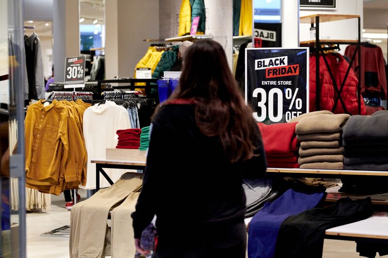 Foto de uma mulher de costas em uma loja de roupas, em frente a um cartaz anunciando ofertas de 30% de desconto Foto de uma mulher de costas em uma loja de roupas, em frente a um cartaz anunciando ofertas de 30% de desconto