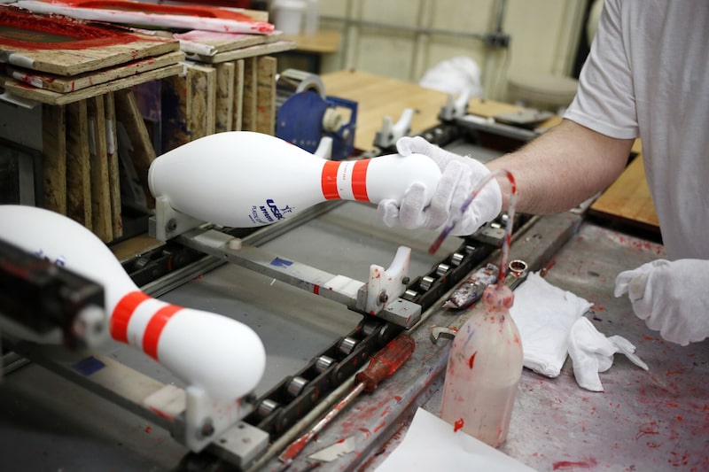 Un trabajador retira unos bolos recién pintados de una cadena de montaje en una fábrica de Lowville, Nueva York. Un trabajador retira unos bolos recién pintados de una cadena de montaje en una fábrica de Lowville, Nueva York.